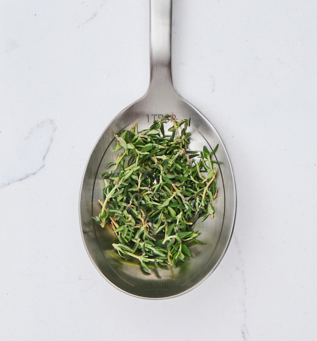 One tablespoon of fresh thyme leaves on stainless steel measuring spoon
